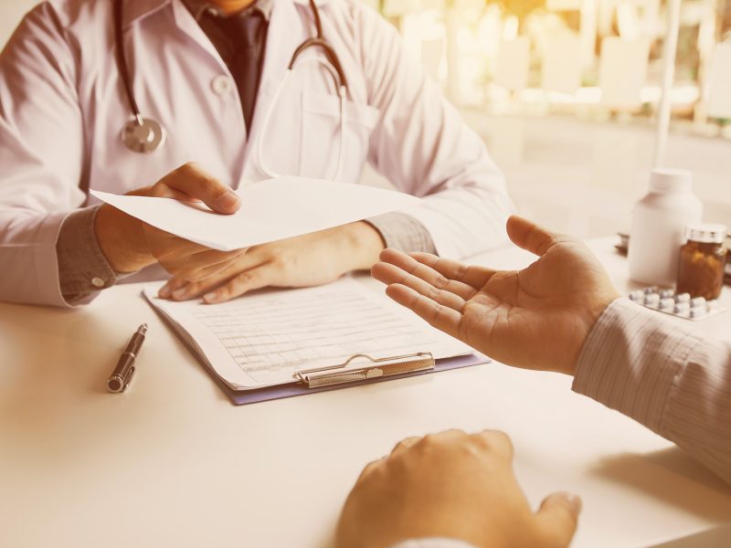 Ein Arzt überreicht einen Arztbrief an den Patienten.